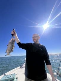 An angler proudly displaying a large Grouper while fishing on a sunny day in open waters.