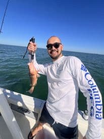 An angler proudly displaying a freshly caught Redfish while fishing on a sunny day in open waters.