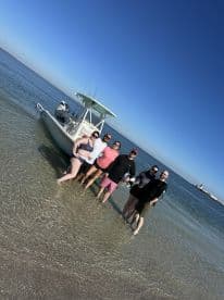 A group of friends enjoying a day on the water, posing in front of their boat in shallow waters, showcasing a beautiful coastal environment.