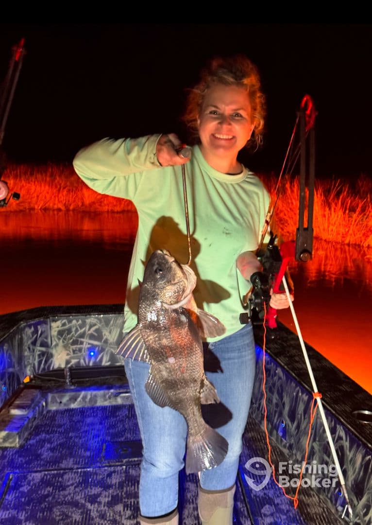Angler proudly displaying a large Black Drum caught at night while fishing from a boat.