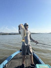 Angler holding a large Largemouth Bass while fishing on a lake, showcasing a successful catch in a scenic outdoor setting.