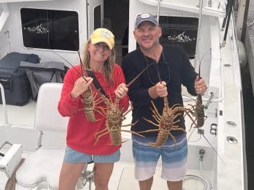 Two anglers proudly displaying their catch of lobsters aboard a fishing boat, showcasing a successful day on the water.