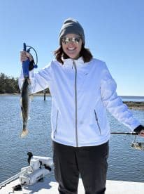 An angler proudly displaying a Speckled Trout while fishing on a sunny day in a coastal waterway.