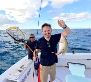 Angler proudly displaying a Snapper caught while fishing offshore, with another crew member in the background.