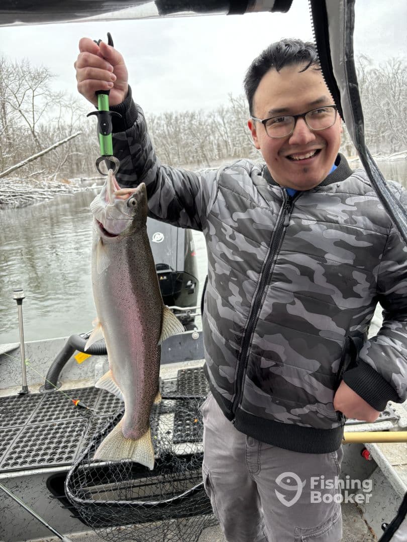 Angler proudly displaying a large Rainbow Trout while fishing on a chilly day, showcasing the excitement of a successful catch.