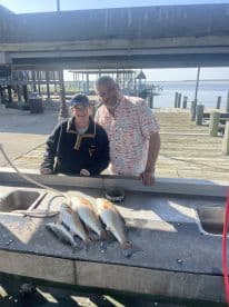 Two anglers smiling at a cleaning station, showcasing their catch of Redfish and Speckled Trout after a successful fishing trip.