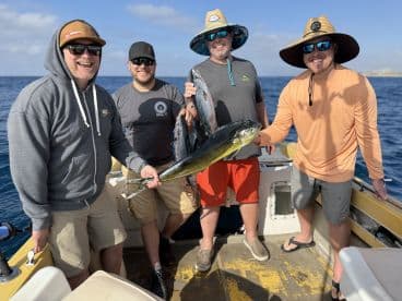 Group of anglers celebrating their catch of a vibrant Mahi Mahi aboard a fishing boat in clear blue waters.