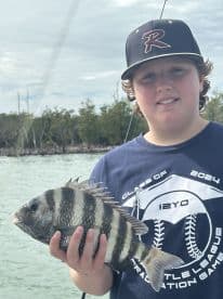 A young angler proudly displaying a Sheepshead caught during a fishing trip, surrounded by a scenic coastal backdrop.