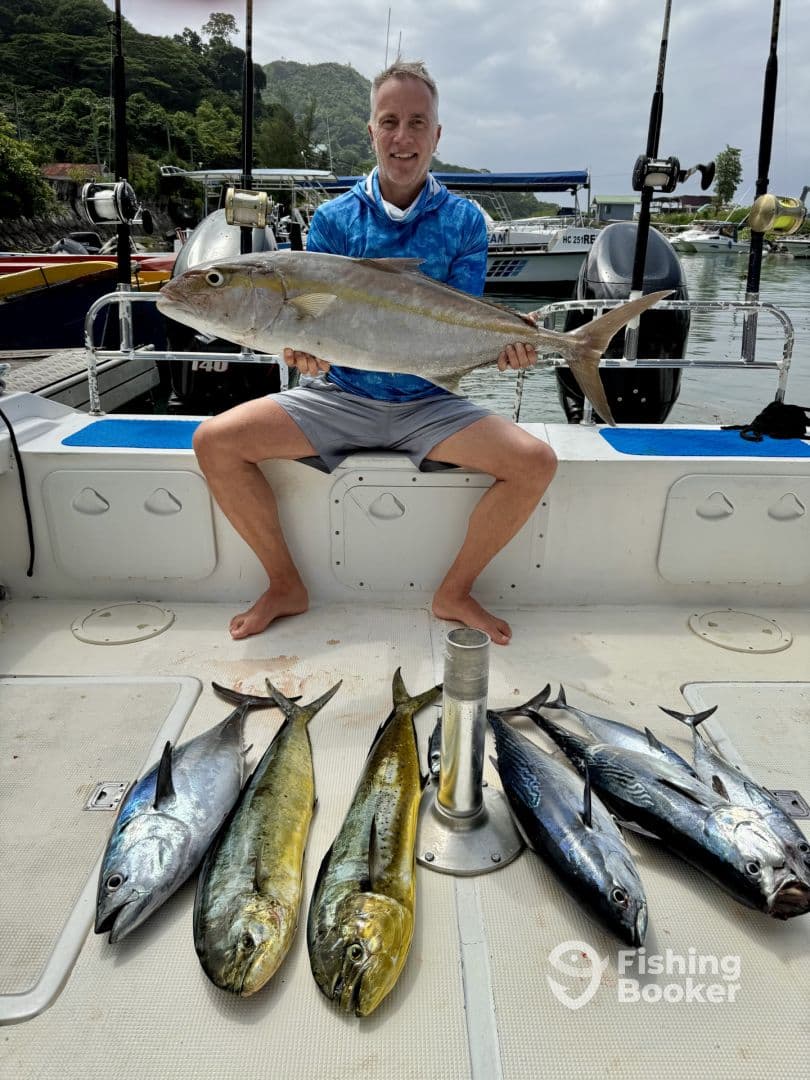 An angler proudly displaying a large Amberjack alongside a variety of Mahi Mahi and Tuna on the deck of a fishing boat, showcasing a successful day out on the water.