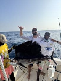 Two anglers proudly displaying a large Sailfish aboard a sport fishing boat, showcasing a successful deep-sea fishing trip.
