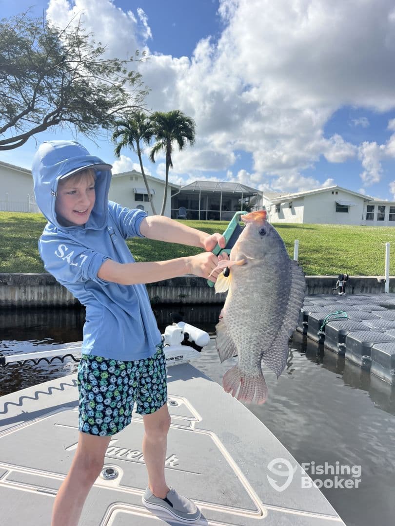 Young angler proudly displaying a large Tilapia on a boat dock, showcasing a successful fishing trip.
