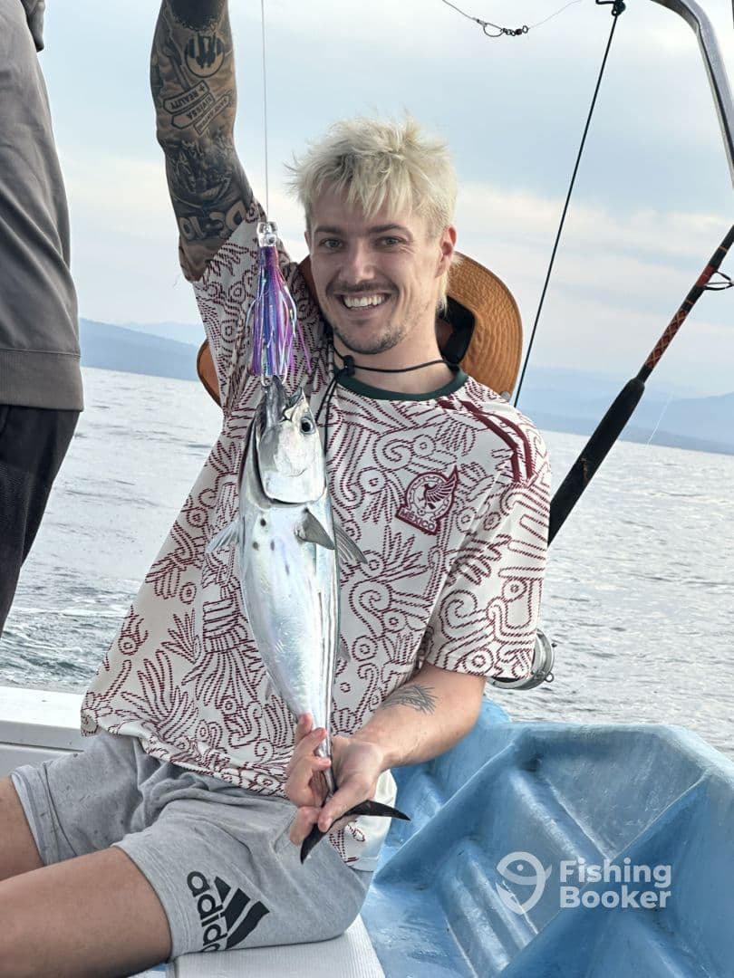 Angler displaying a freshly caught fish while fishing on a boat in open waters.