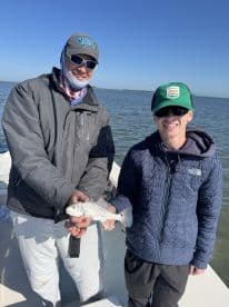 A young angler and an adult proudly displaying a caught fish while on a fishing trip, showcasing a beautiful day on the water.