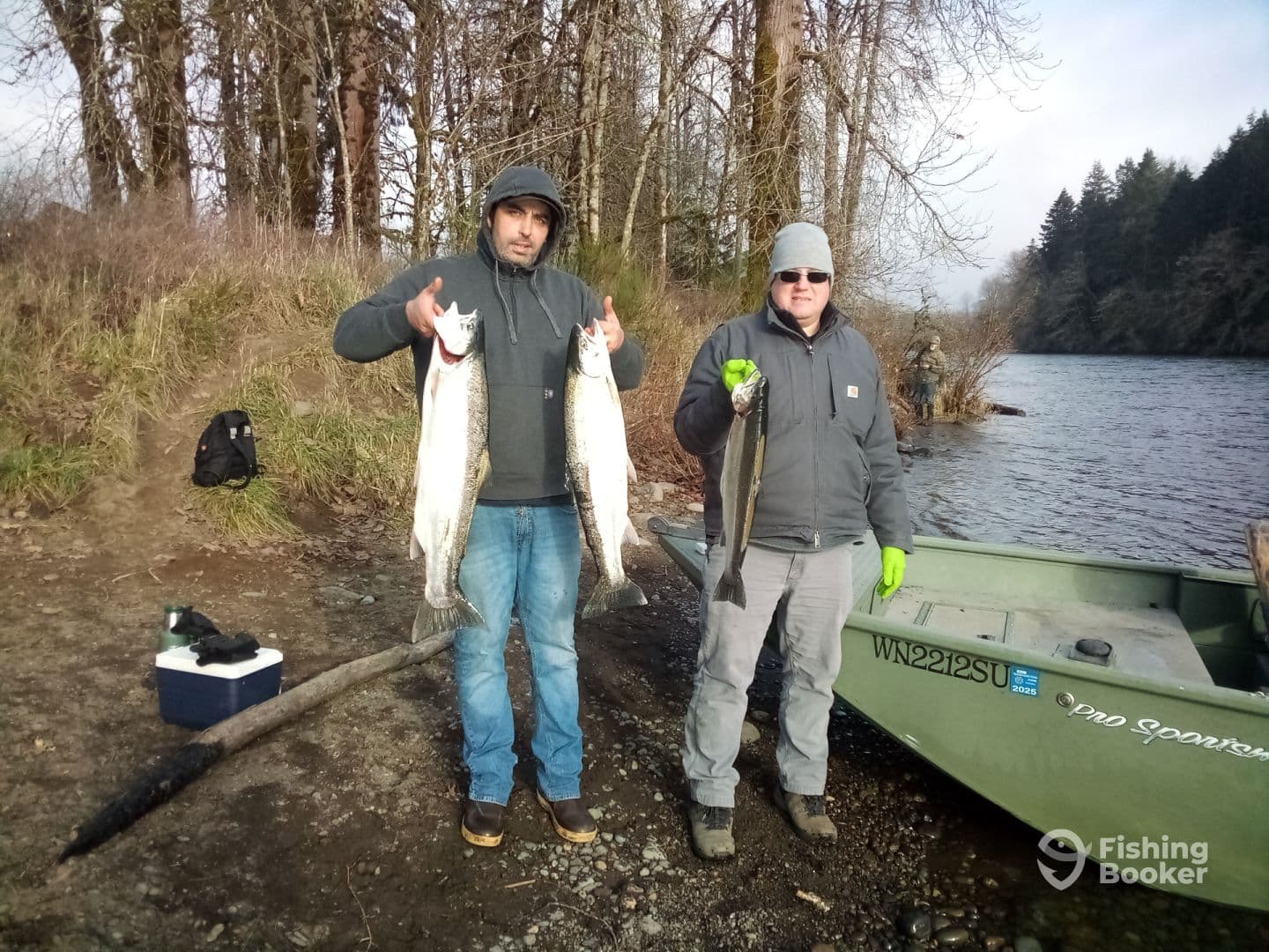 Two anglers proudly displaying their catch of Salmon by the riverbank, with a fishing boat visible in the background.