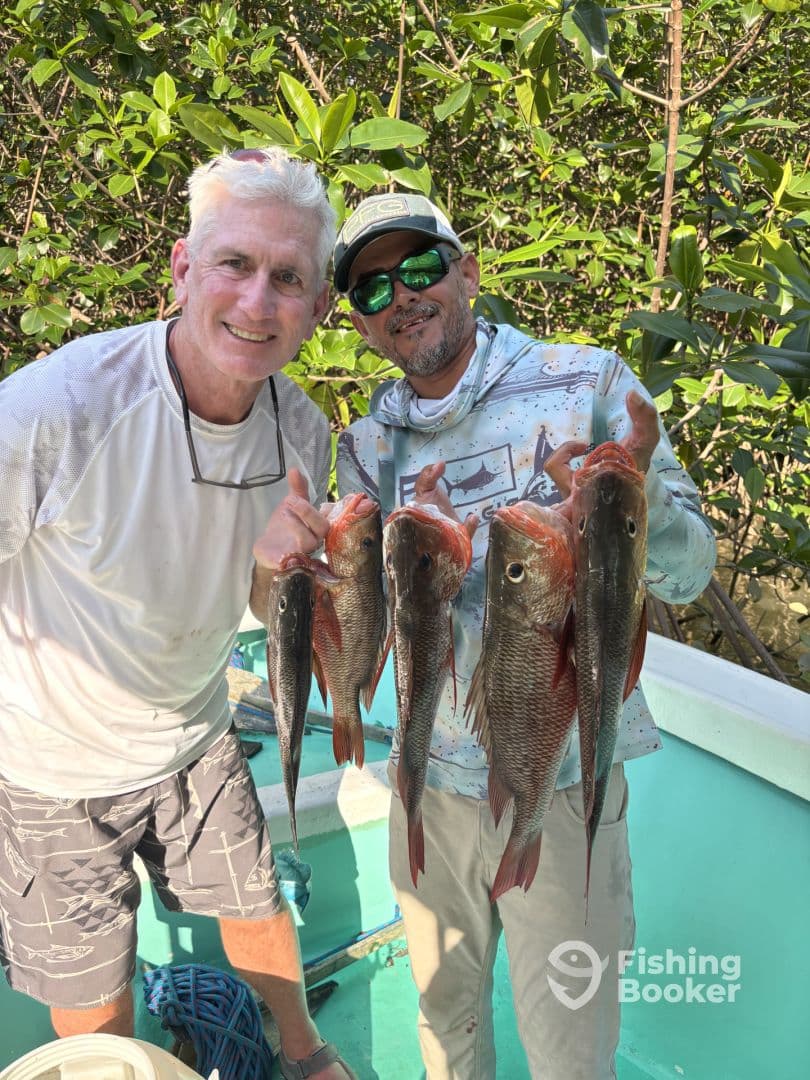 Two anglers proudly displaying their catch of Red Snapper after a successful fishing trip in a tropical setting.