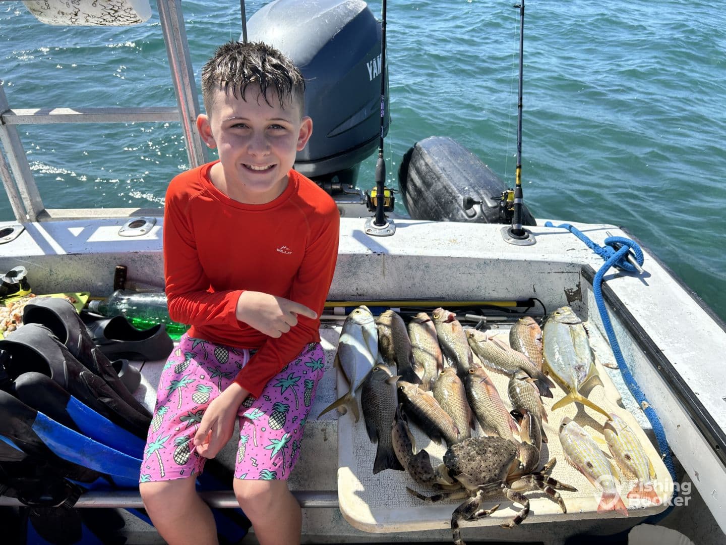 A young angler proudly displaying a variety of fish and a crab on a boat after a successful fishing trip.