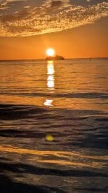 A stunning sunset over the water, reflecting golden hues on the surface, with an island silhouette in the distance.
