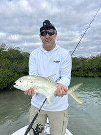 Angler proudly displaying a Silver Jack while fishing in a mangrove area, showcasing a successful catch during a charter trip.