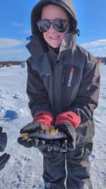 A young angler proudly displaying a colorful perch while ice fishing on a snowy landscape.