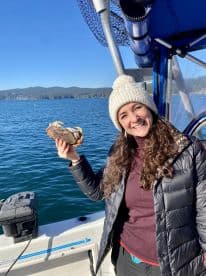 A smiling angler proudly displaying a freshly caught crab while aboard a fishing boat in a scenic coastal environment.