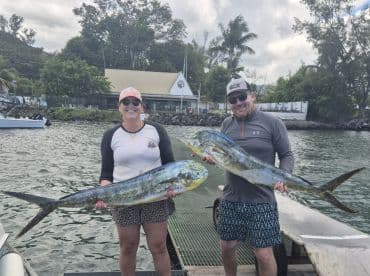 Two anglers proudly displaying their catch of Mahi Mahi at a dockside location, showcasing a successful fishing trip.