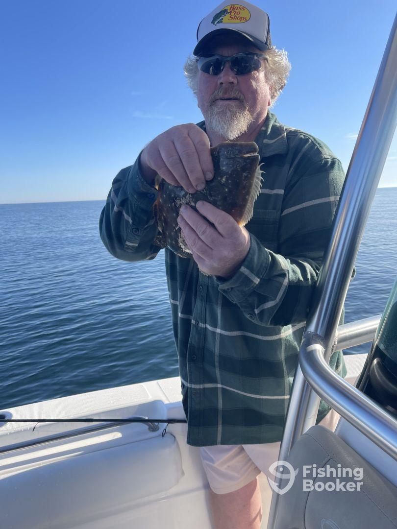 An angler proudly displaying a Flounder while fishing on a calm day at sea.