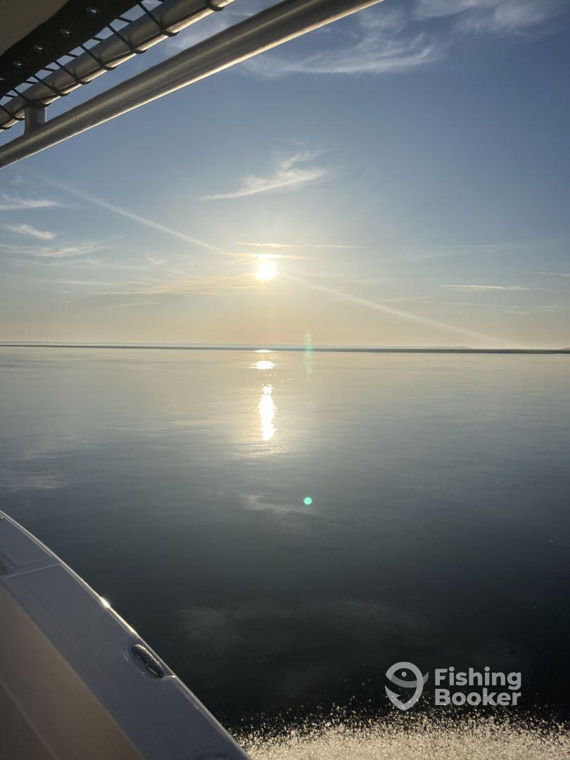 A serene view of the water and sunset from the side of a boat, showcasing a calm fishing environment.