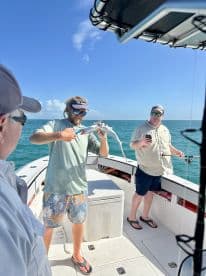 Angler skillfully handling a small shark while fishing on a boat, with two companions observing the action in a sunny coastal environment.