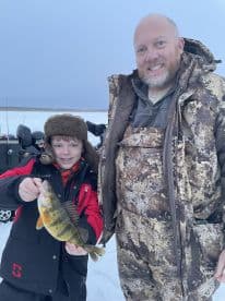 A young angler and an adult proudly displaying a freshly caught Yellow Perch while ice fishing, showcasing a family fishing experience.