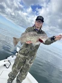 Angler displaying a large Grouper while fishing on a calm day in open waters.