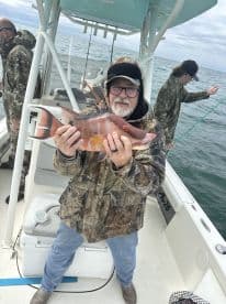 An angler proudly displaying a colorful Red Snapper while fishing on a boat in open waters.