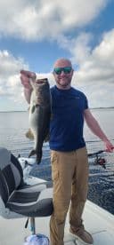 An angler proudly displaying a large Largemouth Bass while fishing on a calm lake, showcasing a successful day on the water.