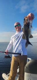 Angler proudly displaying a large Largemouth Bass while fishing from a boat on a calm lake.