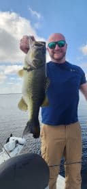 An angler proudly displaying a large Largemouth Bass while fishing on a boat, showcasing a beautiful day on the water.