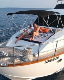 A couple relaxing on the bow of a luxury yacht, enjoying the serene ocean view during a sunny day.