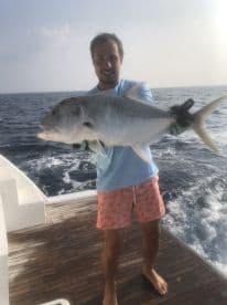 An angler proudly displaying a large Trevally while fishing offshore, showcasing the excitement of a successful catch.