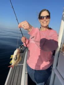 An angler proudly displaying a colorful fish while fishing on a calm day at sea.