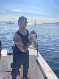 Angler displaying a freshly caught fish while aboard a boat in calm waters, showcasing a successful fishing trip.