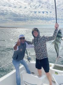 Two anglers celebrating a successful catch of a large fish while aboard a boat, showcasing a beautiful ocean backdrop.