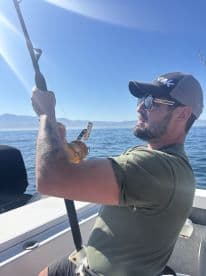 An angler actively reeling in a catch while fishing on a sunny day, showcasing the excitement of the sport in a scenic marine environment.