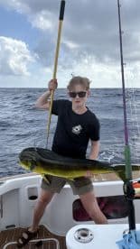 Young angler proudly holding a large Mahi Mahi while fishing offshore, showcasing a successful catch.