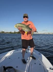 An angler proudly displaying a large Jack Crevalle while standing on the bow of a boat, enjoying a day of fishing in calm waters.