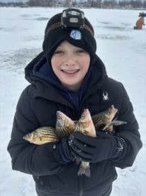A young angler proudly displaying multiple striped bass while ice fishing on a snowy lake.