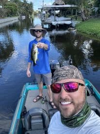 Two anglers enjoying a day of fishing on a calm waterway, with one proudly displaying a large Largemouth Bass.