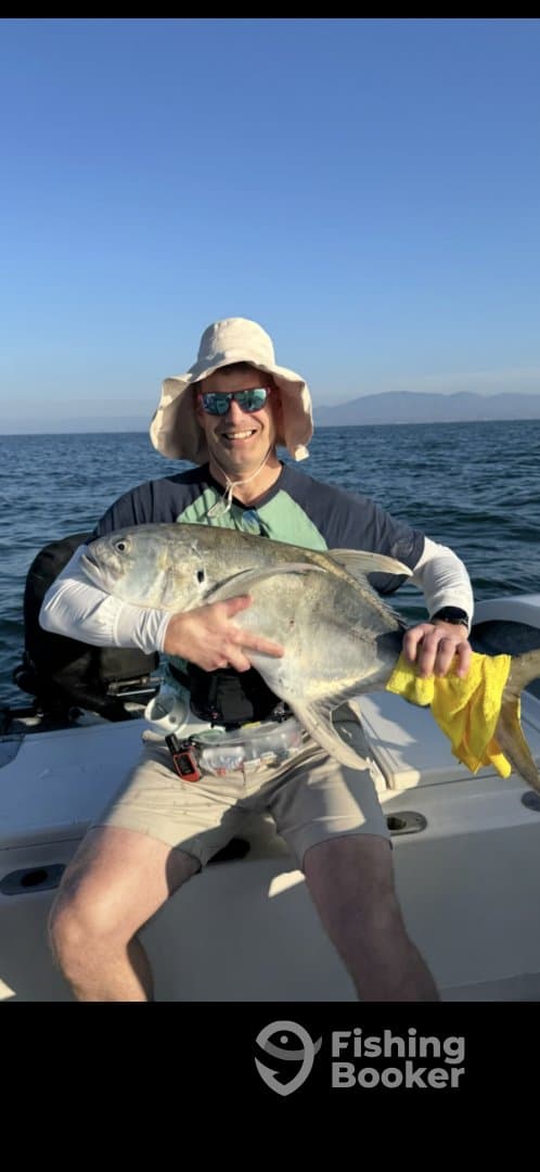 Angler proudly displaying two large Jack Crevalle while fishing on a boat in a sunny coastal environment.