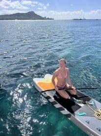 A young woman enjoying paddleboarding in clear waters with a scenic backdrop of Diamond Head in Hawaii.