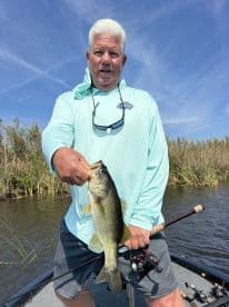 An angler proudly displaying a large Largemouth Bass while fishing from a boat in a scenic freshwater environment.