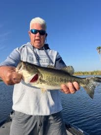 An angler proudly displaying a large Largemouth Bass while fishing on a calm waterway, showcasing a successful day on the water.