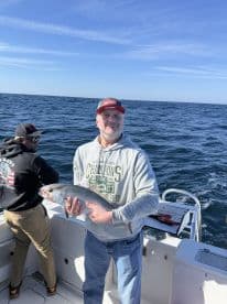 An angler proudly displaying a freshly caught fish while fishing on a boat in open waters.