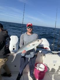 An angler proudly displaying a large Amberjack while fishing offshore, showcasing a sunny day on the water.